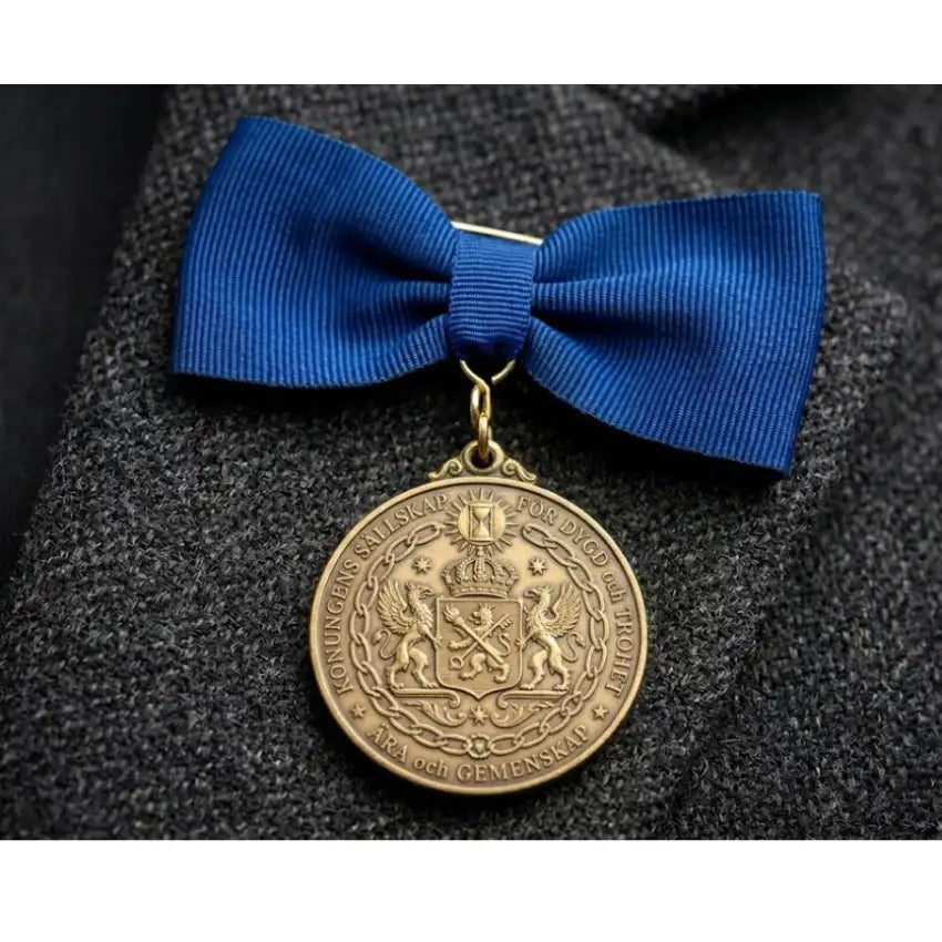 Kort medaljband i blått tyg med rosettform och guldfärgad medalj i metall.